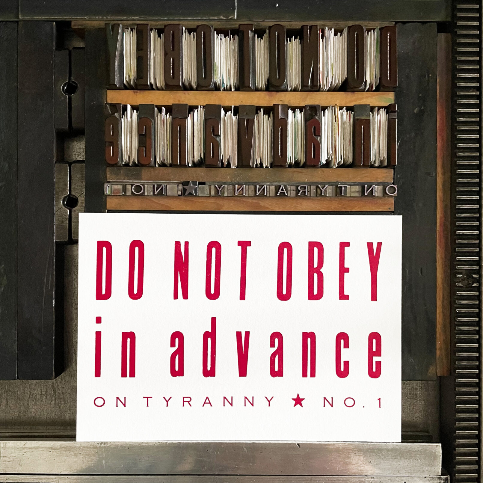 Image of printed letterpress print on Vandercook press bed. Printed in red ink, the print reads "Do Not Obey in Advance On Tyranny No. 1"