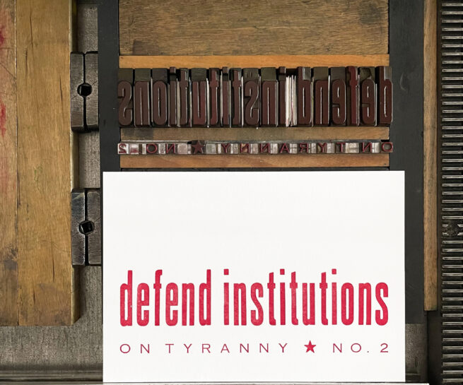 Letterpress print on Vandercook press bed. Printed in red ink on white paper, the text reads "Defend Institutions On Tyranny No. 2."