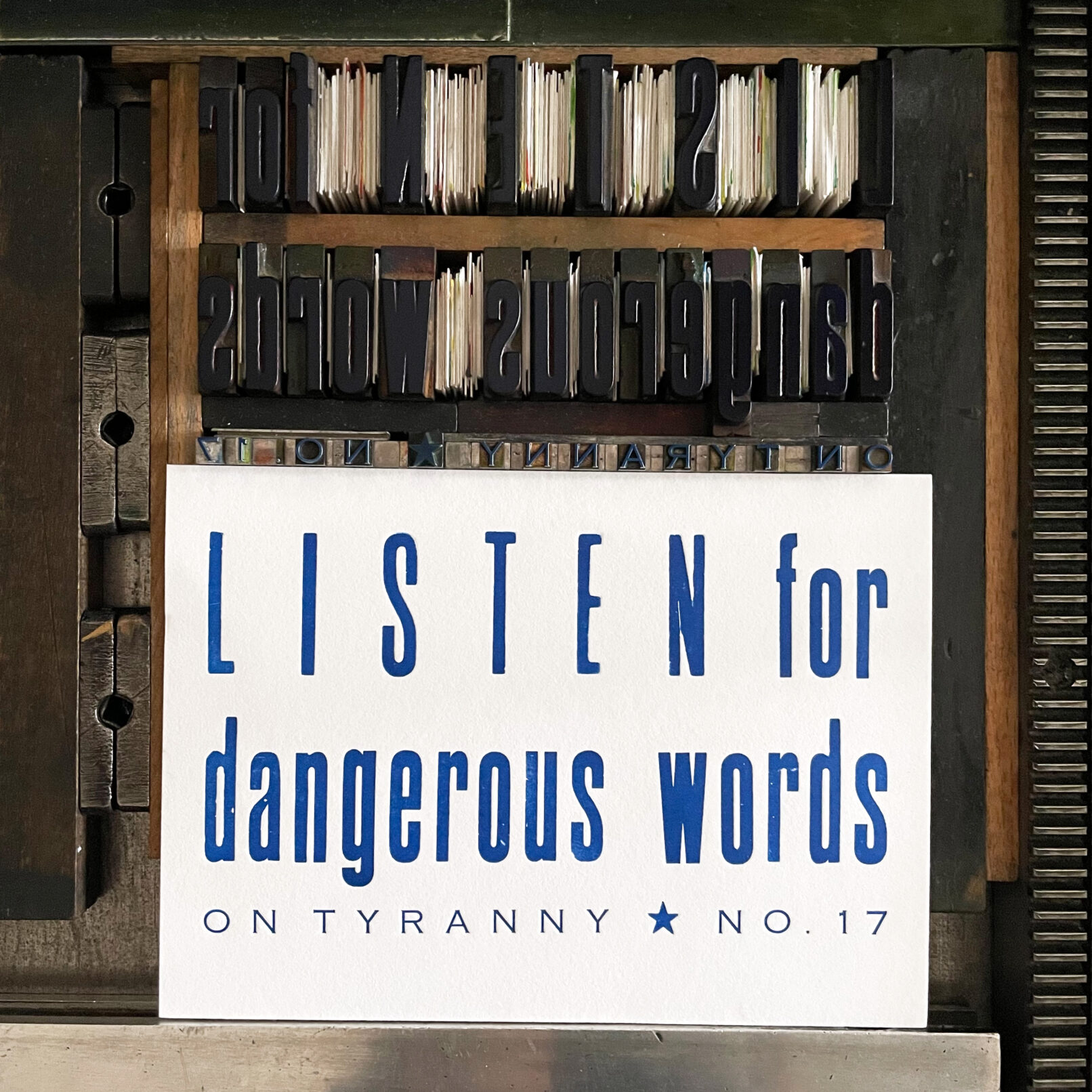 Letterpress print on Vandercook press bed. Text printed in blue ink on white paper that reads "Listen for Dangerous Words On Tyranny No. 17"