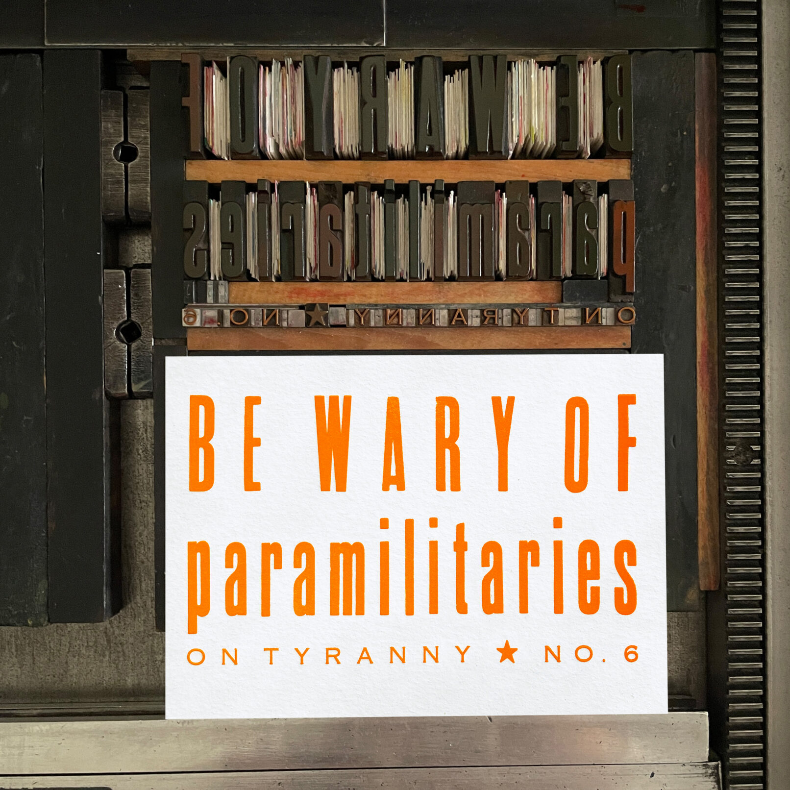 Letterpress print on Vandercook press bed. Printed in orange ink on white paper, the text reads "Be Wary of Paramilitaries On Tyranny No. 6."