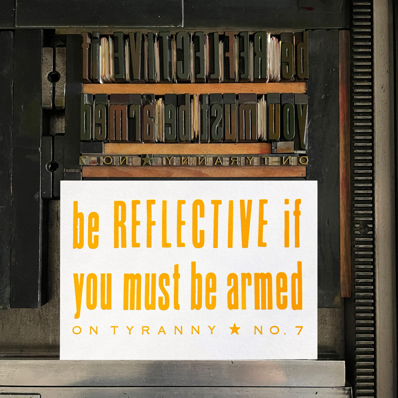Letterpress print on Vandercook press bed. Printed in yellow ink on white paper, the text reads "Be Reflective if You Must Be Armed On Tyranny No. 7."